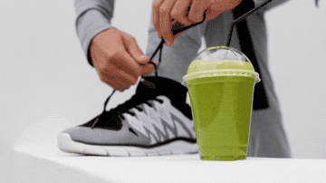 A man ties his running shoe next to a green smoothie
