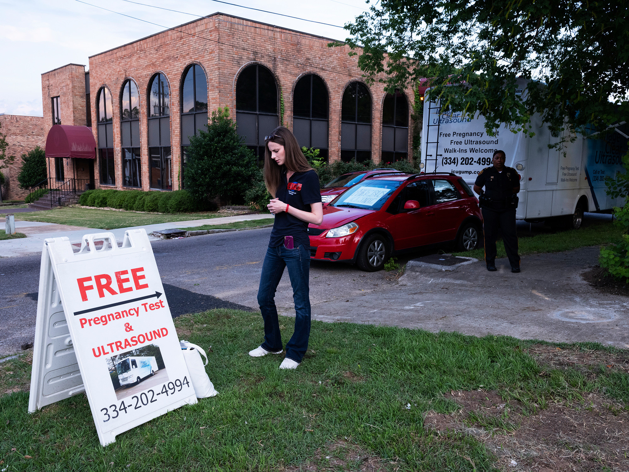 A woman prays near a sign advertising free pregnancy tests and ultrasounds in front of a mobile clinic