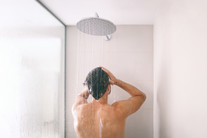 Man taking a shower washing hair with shampoo product under water falling from luxury rain shower head
