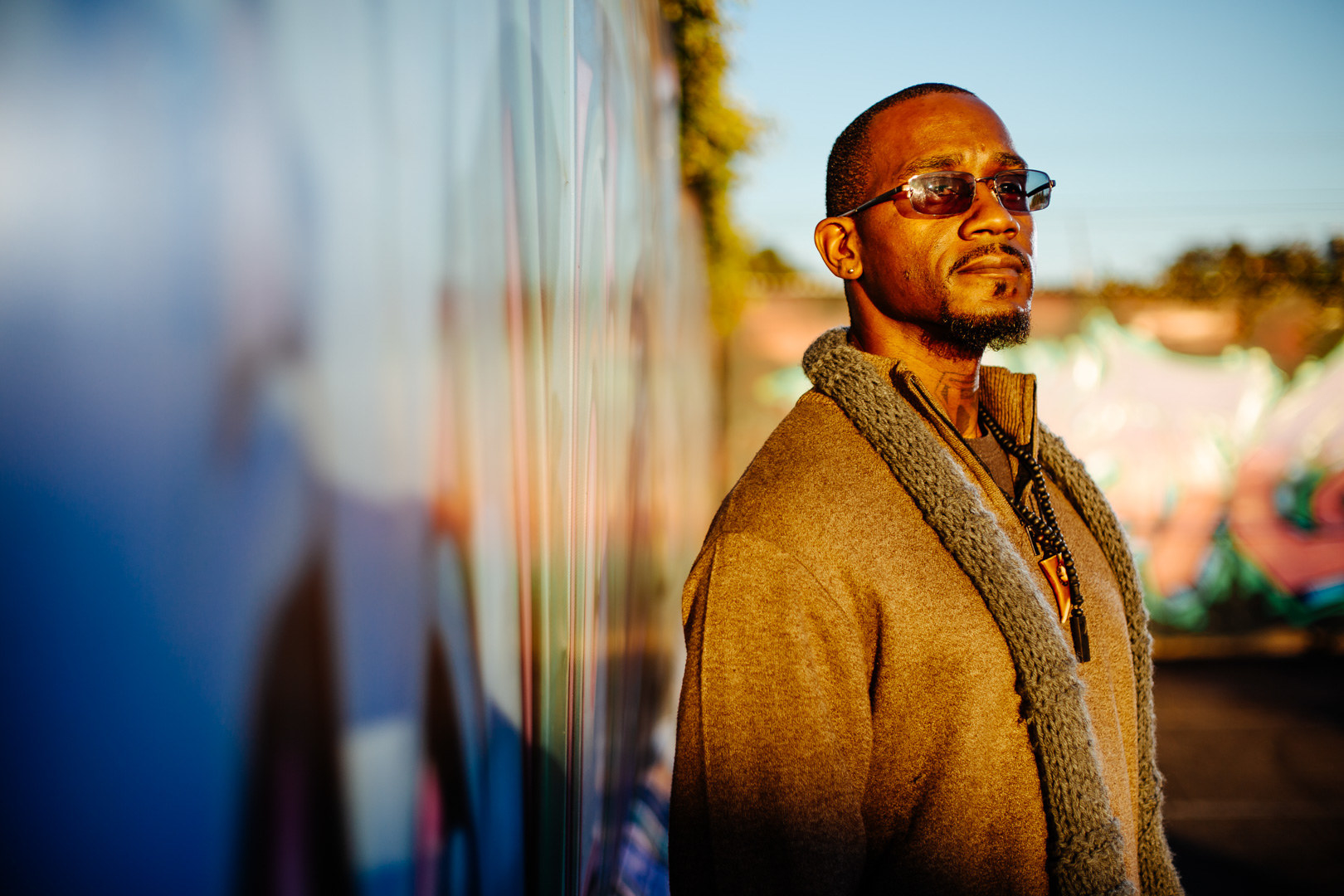 A Black man wearing sunglasses and a scarf looks into the distance