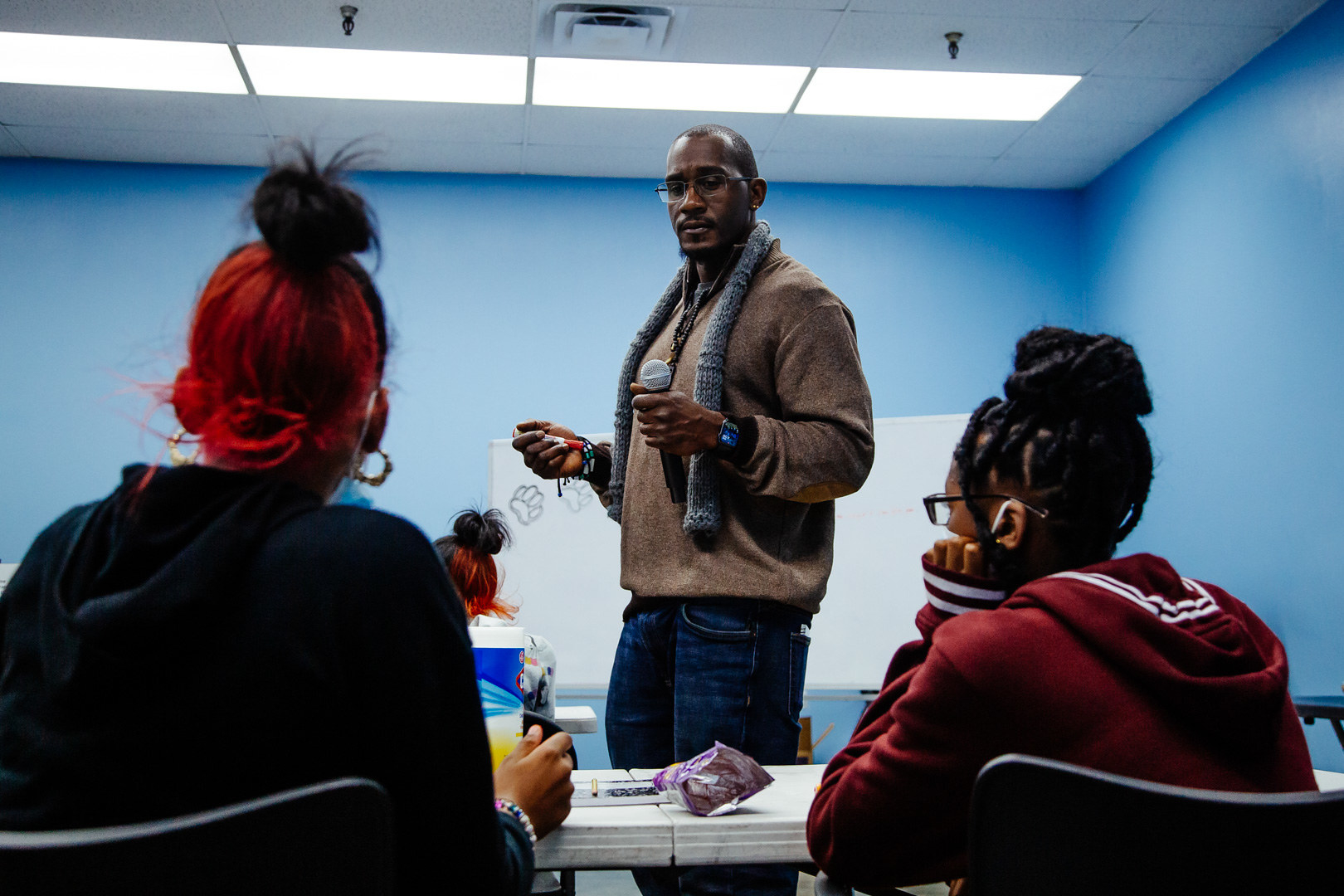 Quinnie, standing, holds a microphone while students sit at a table