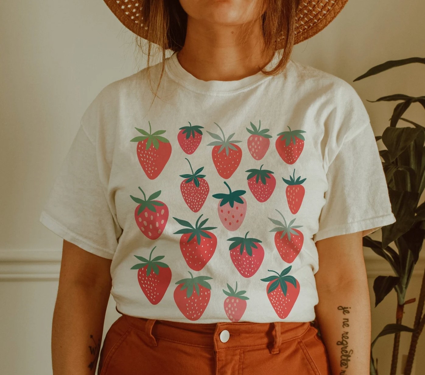 Model is wearing a white tee that has multiple strawberries printed on the front