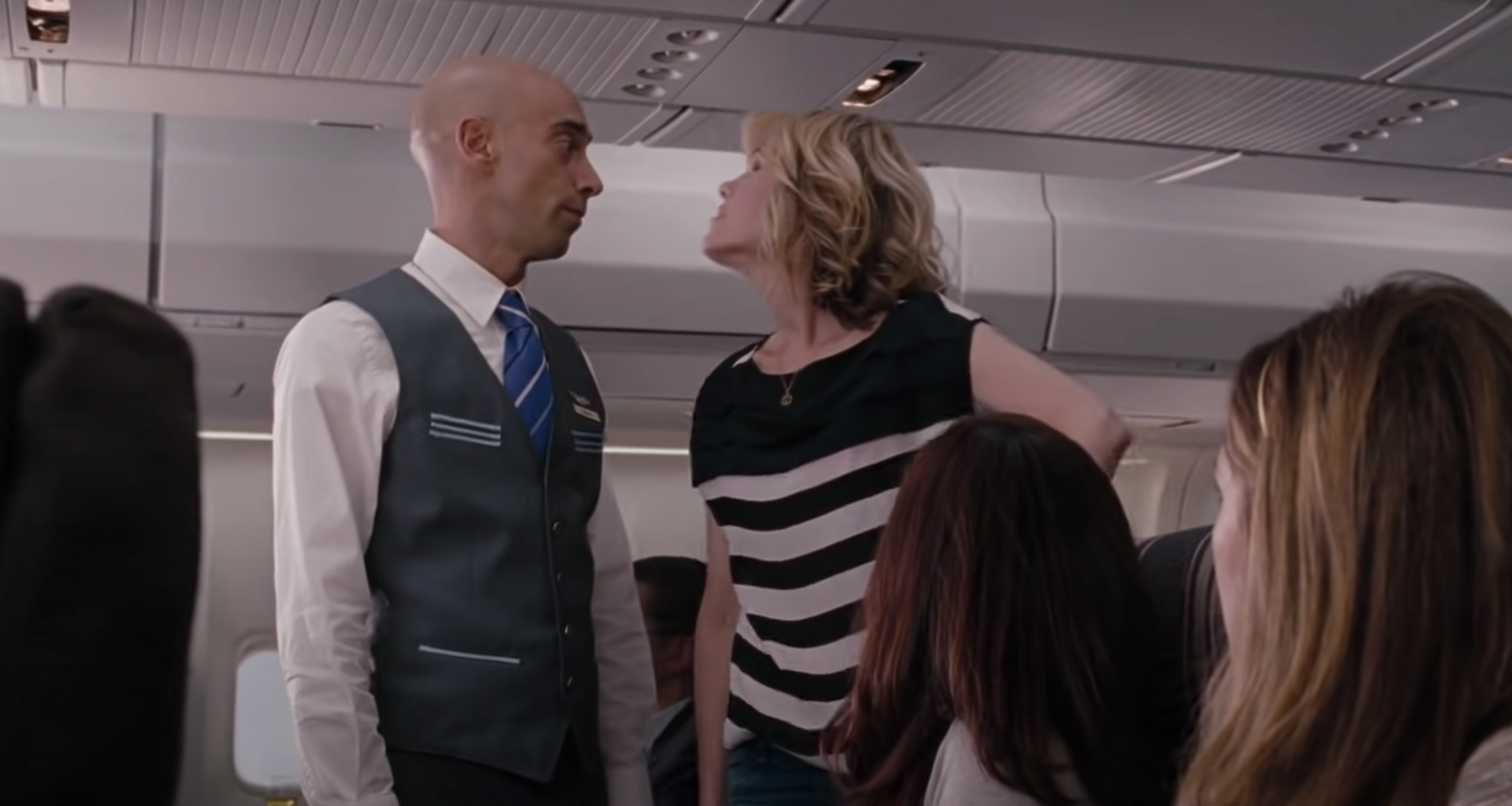 A woman confronts a man in a flight attendant uniform in the plane aisle