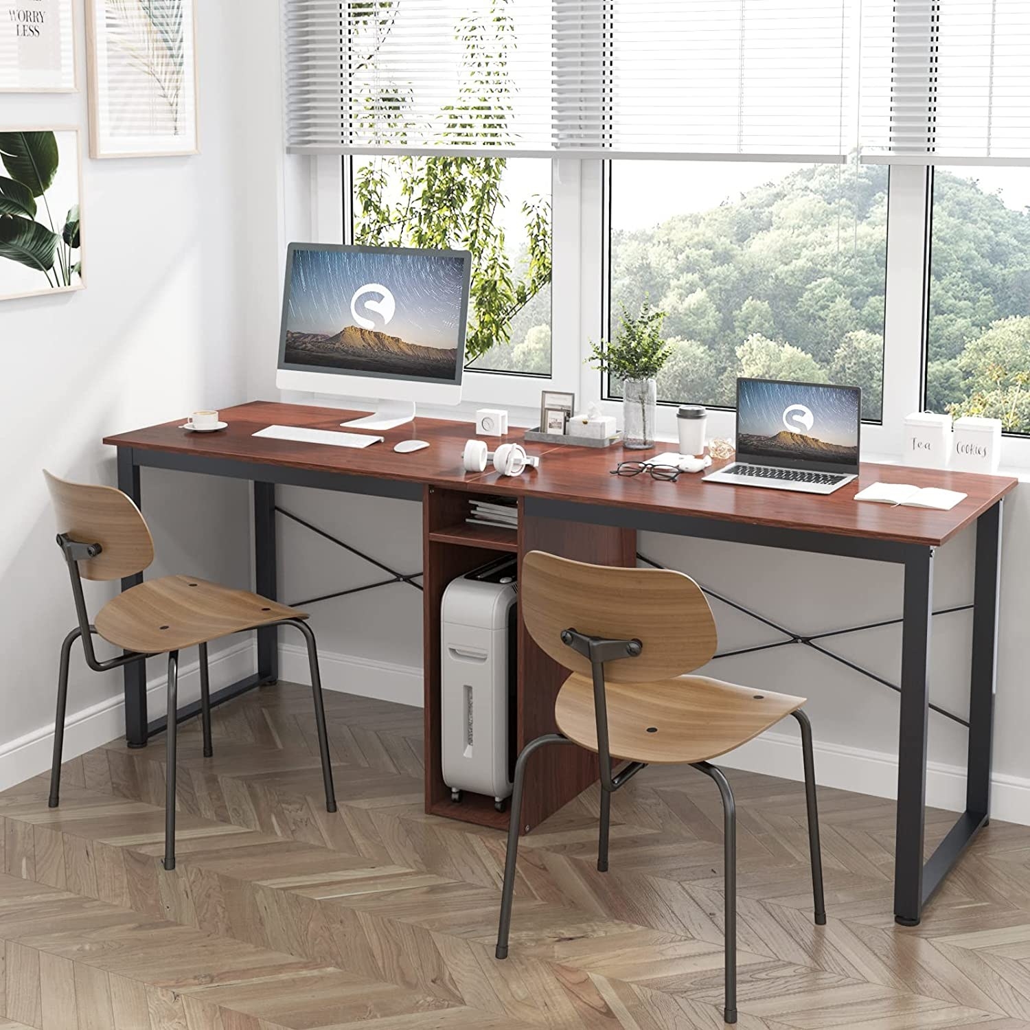 The two-person desk with a monitor and laptop on it and two chairs in front of it