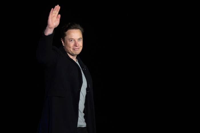 Elon holds his hand up and waves