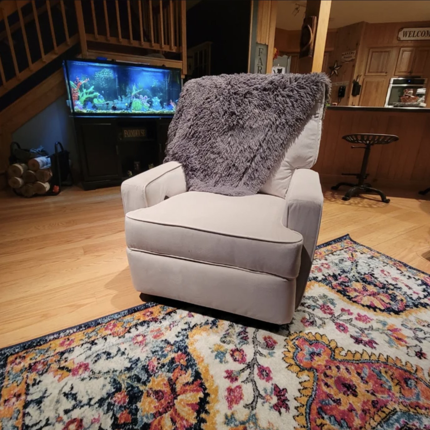 Reviewer&#x27;s photo of the grey chair sitting in living room with a throw blanket draped over it