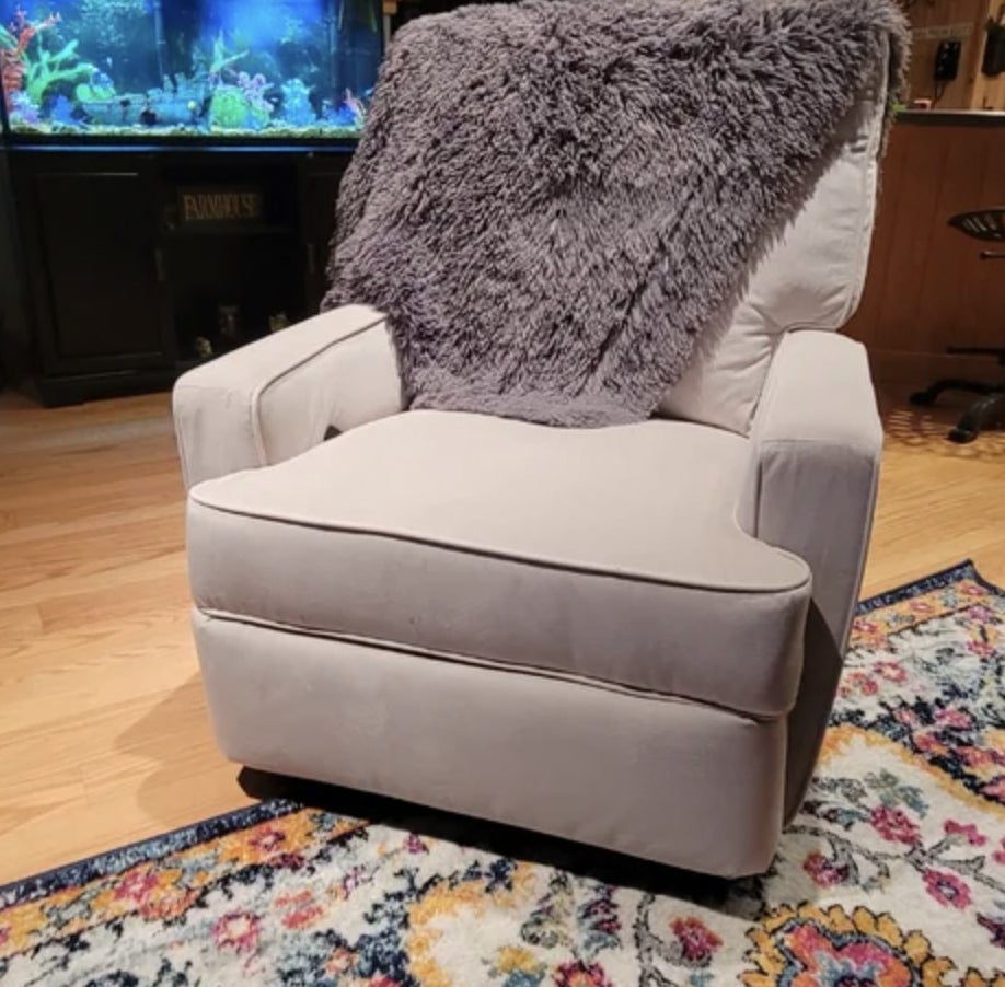 Reviewer&#x27;s photo of the grey chair sitting in living room with a throw blanket draped over it