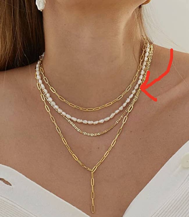 Model is wearing various gold necklaces and a baroque pearl necklace