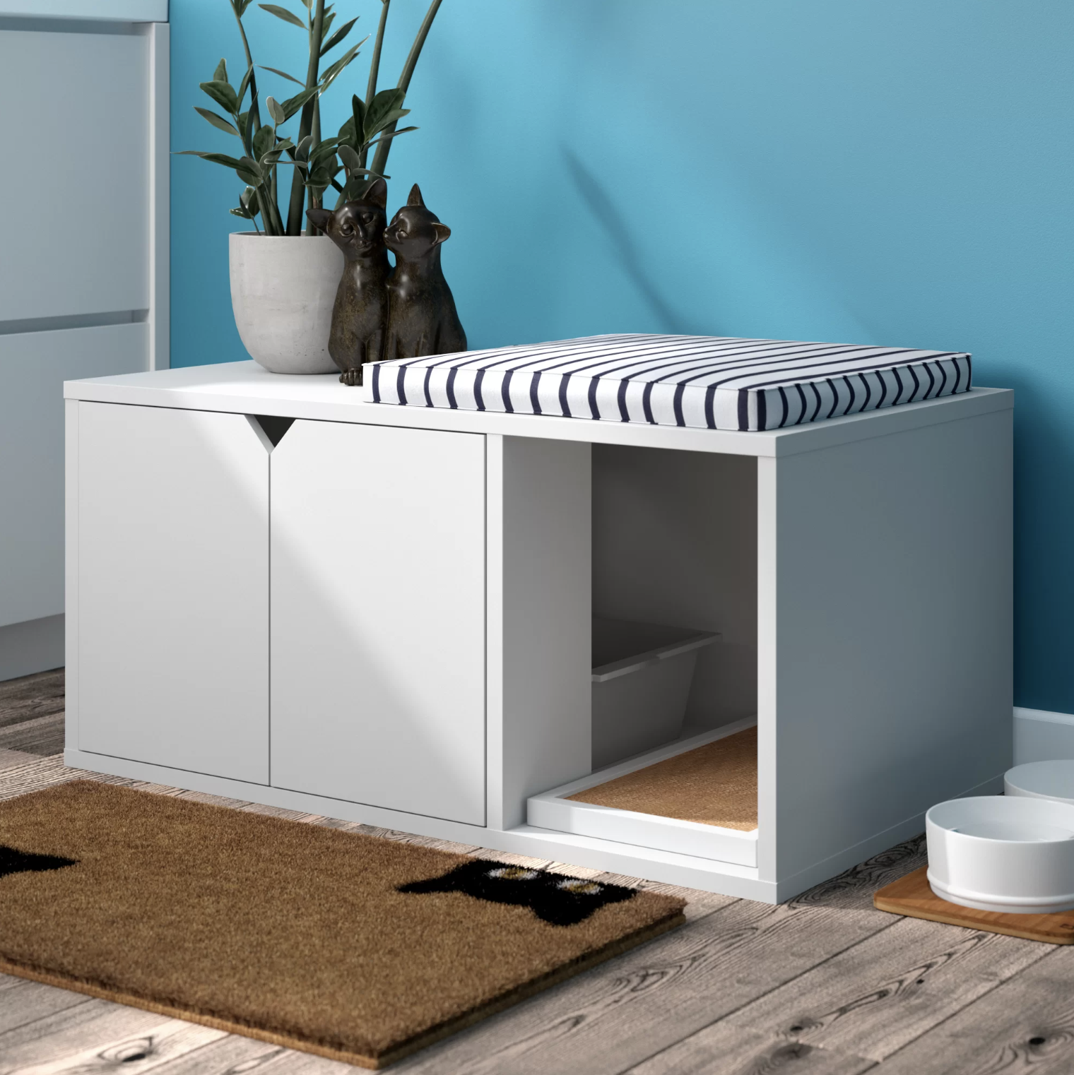 The litter box enclosure with a pillow, cat sculptures, and plant on top of it