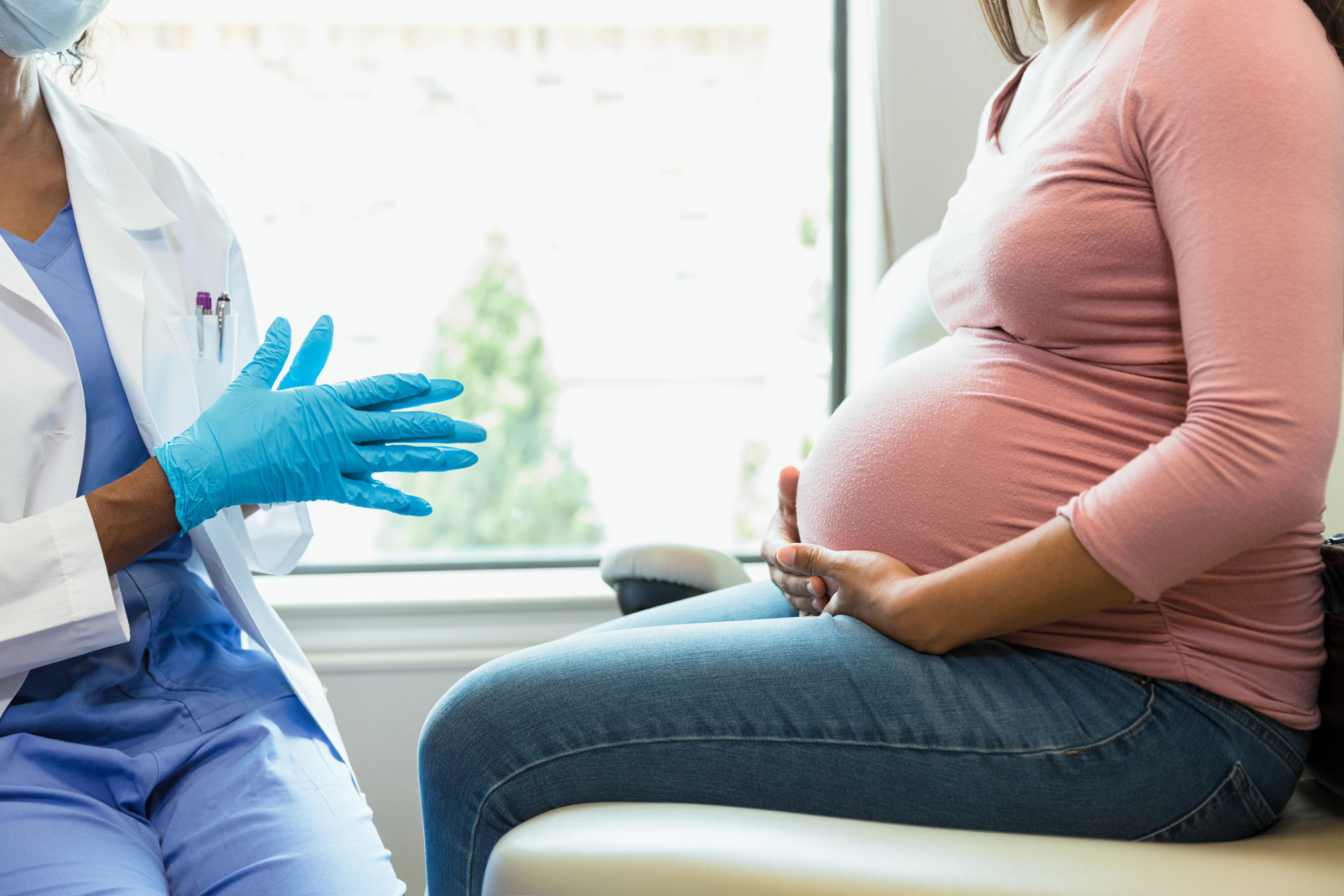 A pregnant woman&#x27;s belly facing a doctor talking to her