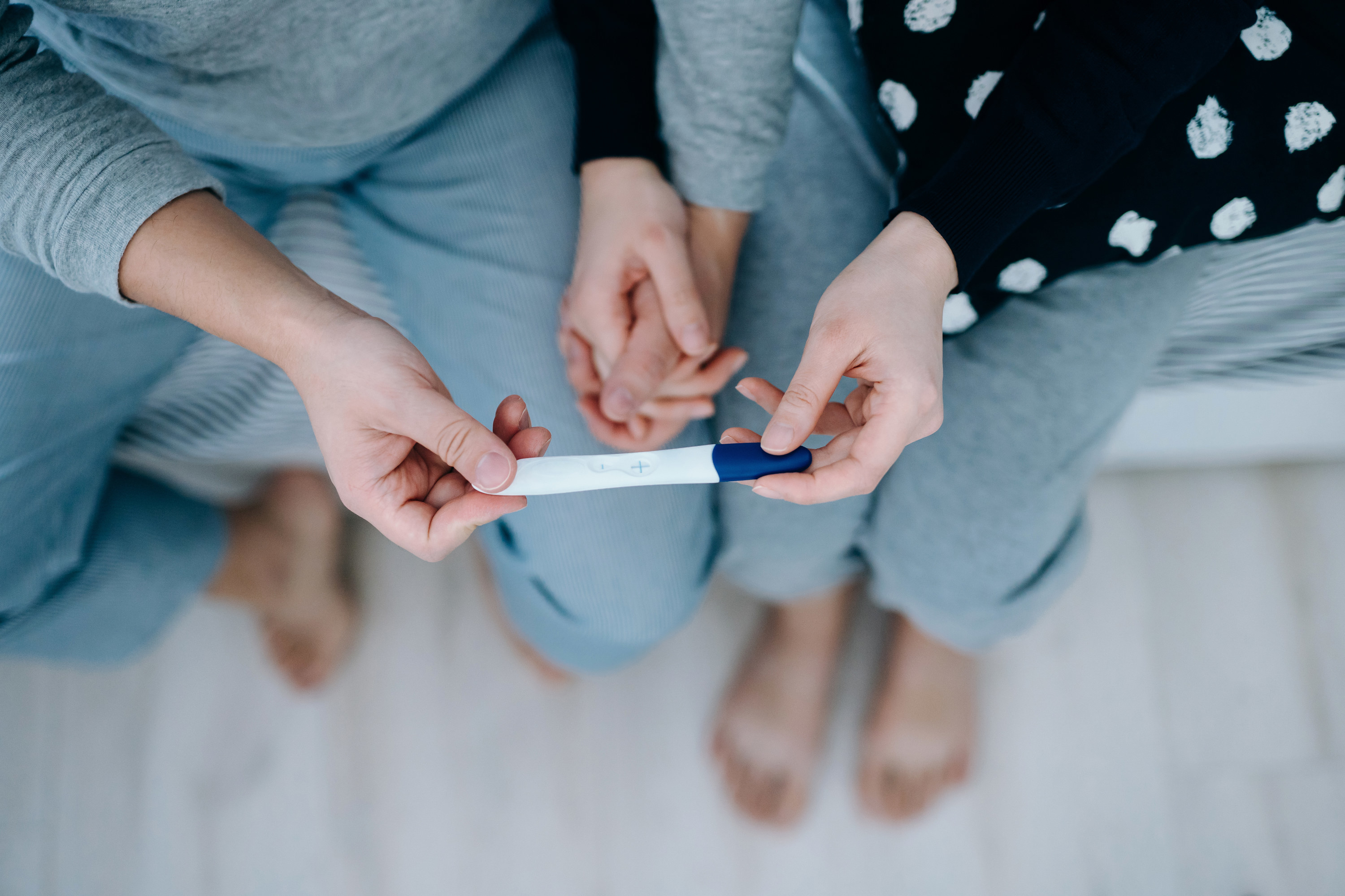 Couple sitting on the bed, holding hands and holding a pregnancy test together