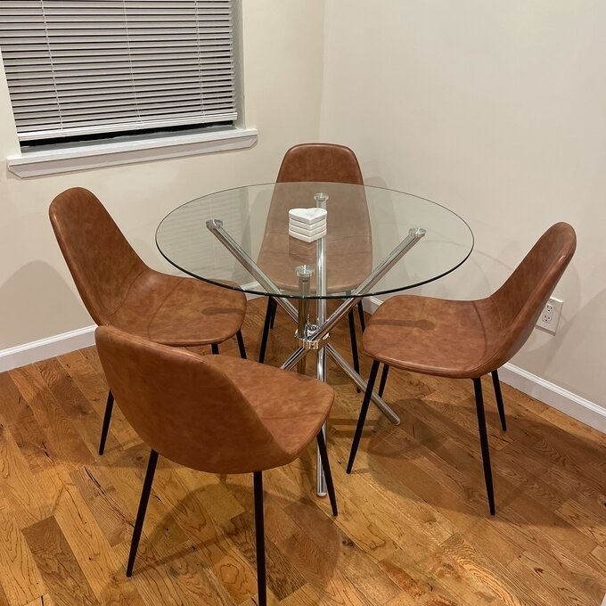 Four brown leather dining chairs around a round white dining table