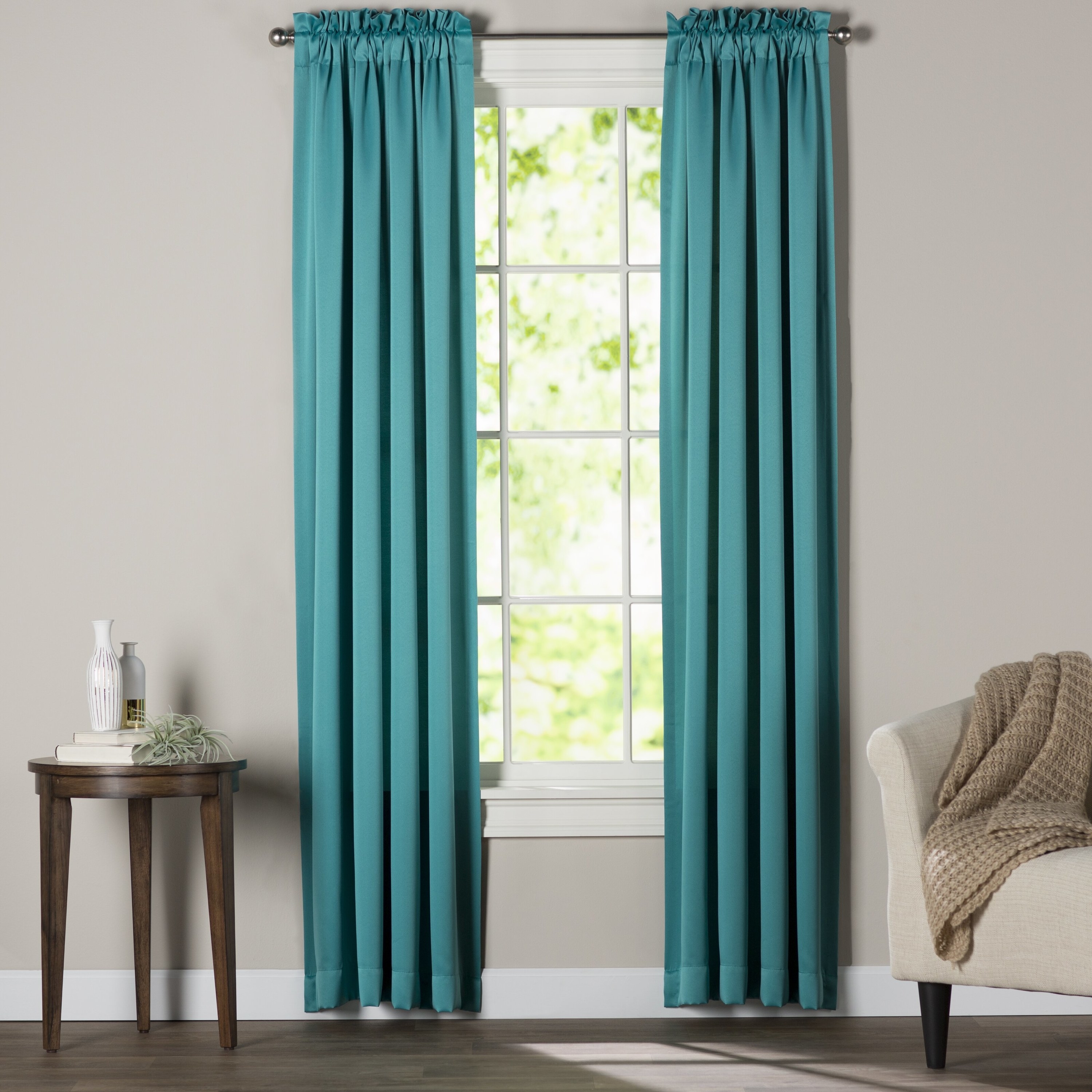 teal curtains on a window next to an armchair, rug and nightstand