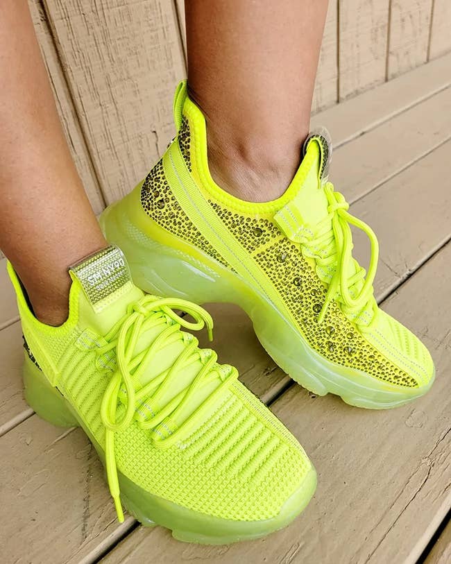 Reviewer neon green bedazzled sneakers against a tan wooden background