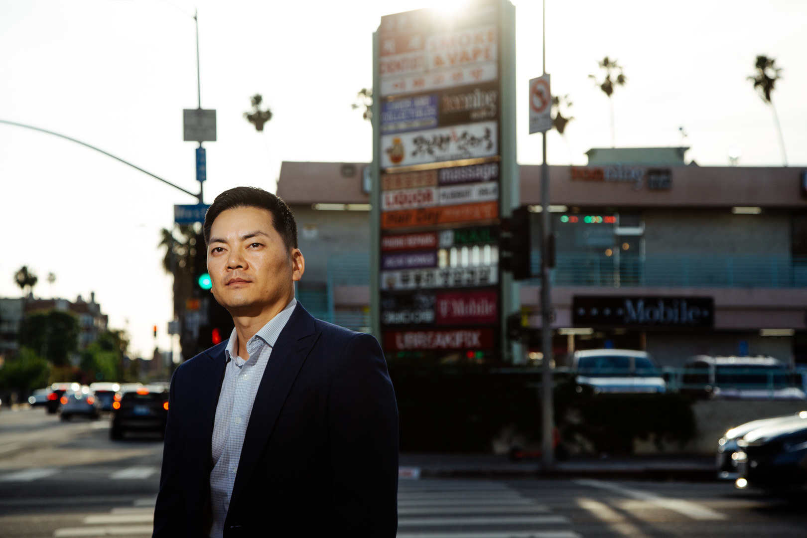 An Asian American man stands across the street from a small shopping complex