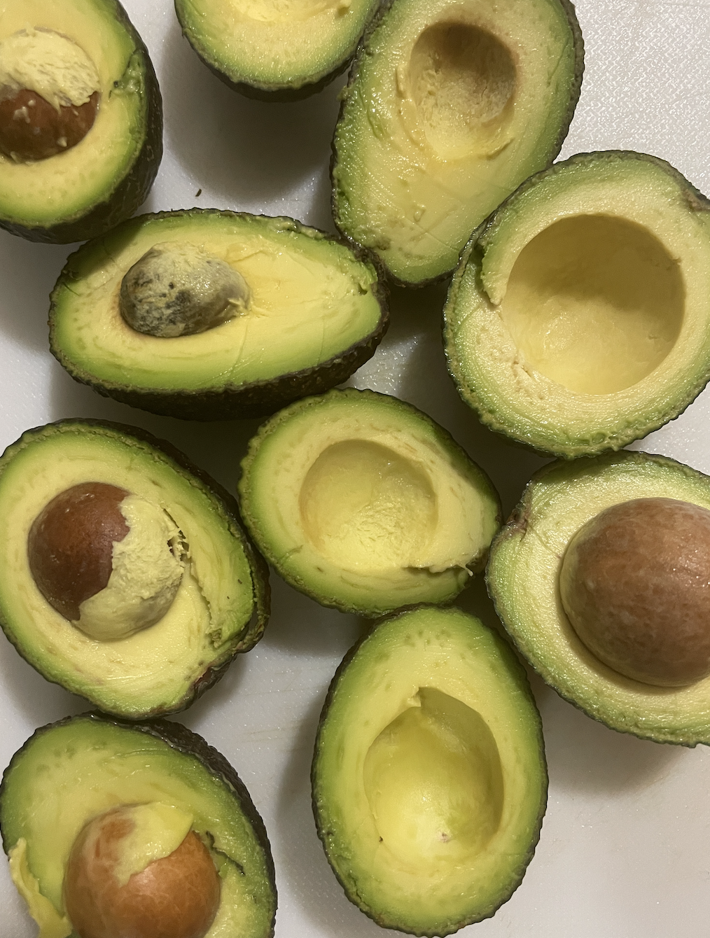 Halved, ripe avocados, some with the pits still inside them