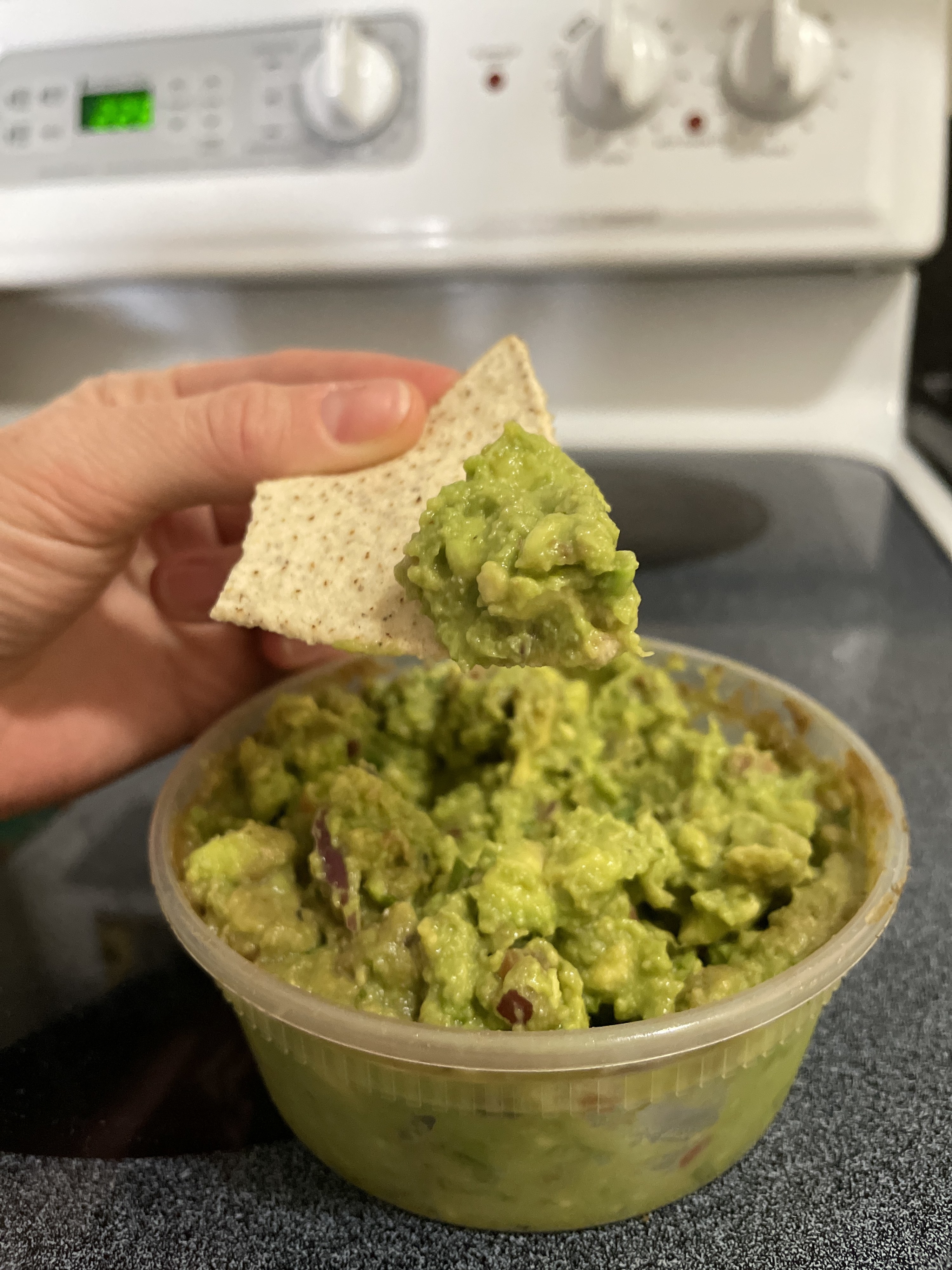 Hand holding a chip with guac on it above a container of guac