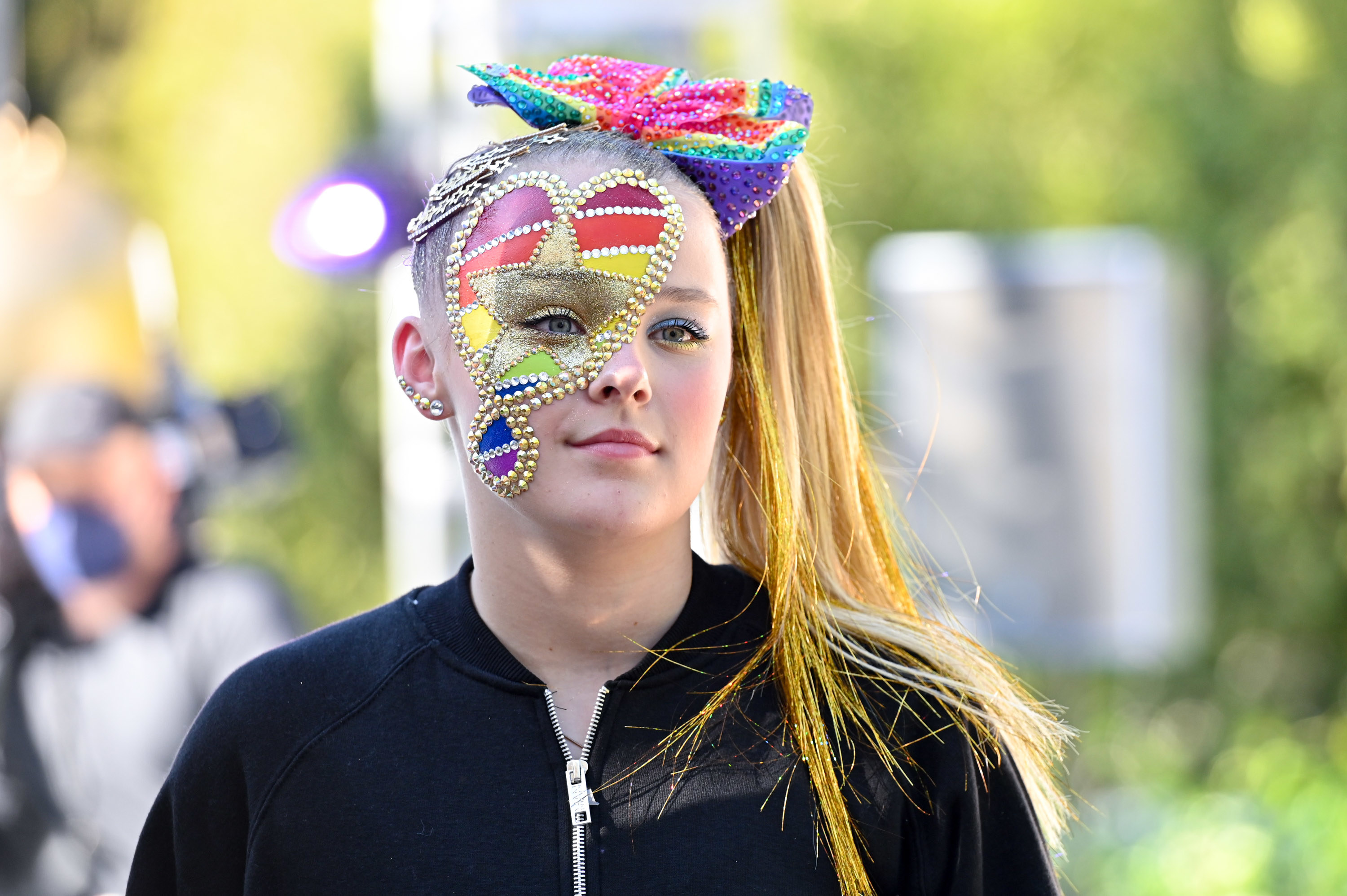 JoJo looks in the distance with her face adorned with a multicolored painted heart