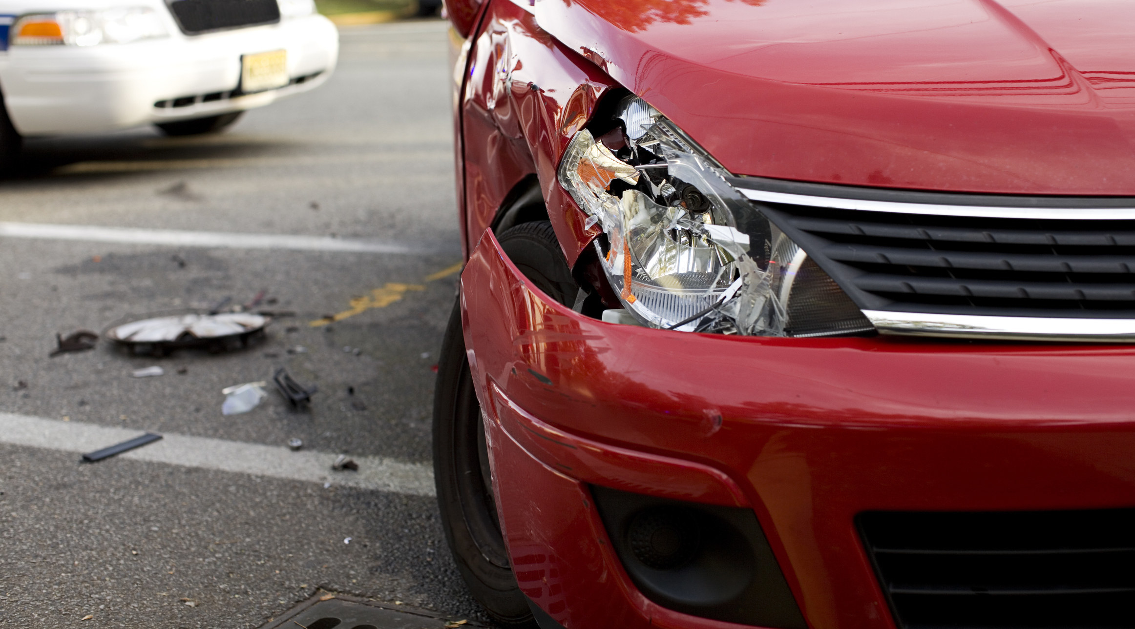 A car sits in the road with a smashed headlight