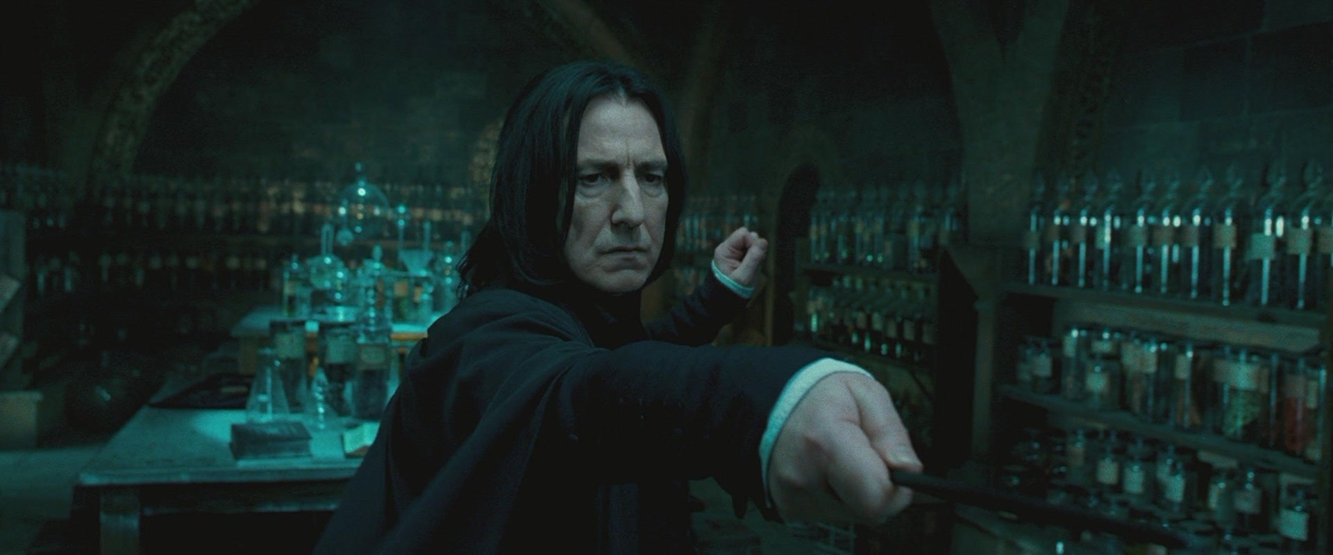 Snape in a dungeon, surrounded by glass bottles, pointing his wand at someone off camera