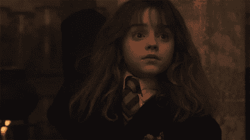 Hermione in a dark classroom, raising her hand eagerly