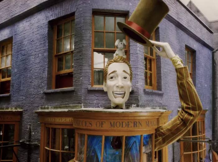 A shot of Fred and George's joke shop, the exterior painted purple with a model of a man taking his hat off
