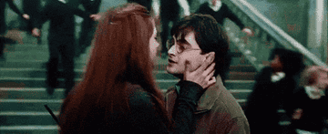 Harry and Ginny kiss at the foot of a staircase while students run all around them