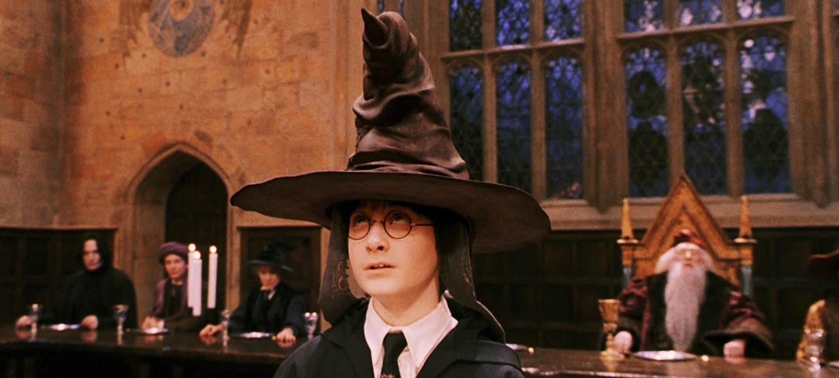 Harry Potter, in his first year, wearing a pointy black hat in the Hogwarts great hall