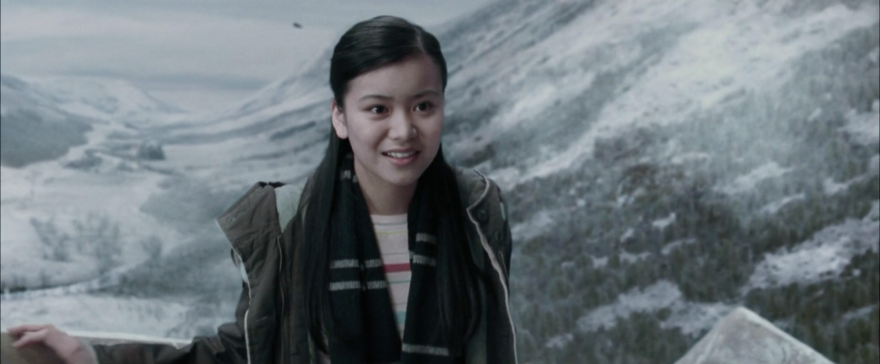 Cho Chang smiling at someone off-scren, while there&#x27;s snow on the mountains behind her