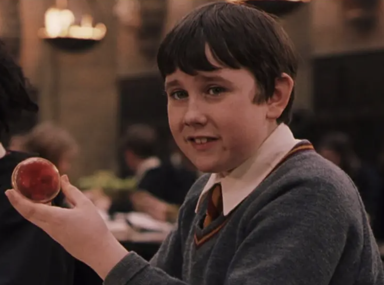 A young Neville Longbottom holding a glass orb filled with red smoke, looking very unsure