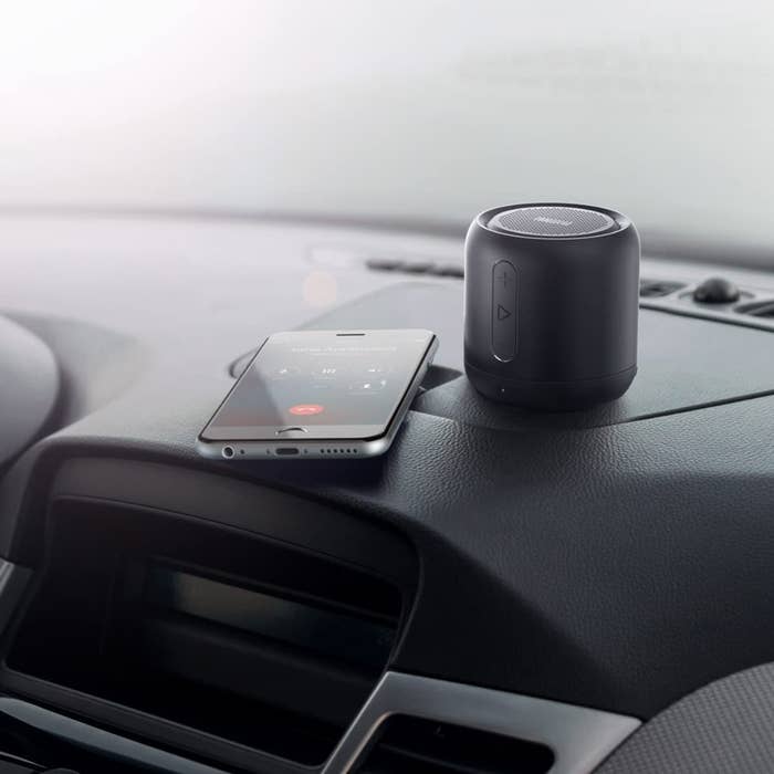 a mini bluetooth speaker next to a cell phone on a dashboard of a car