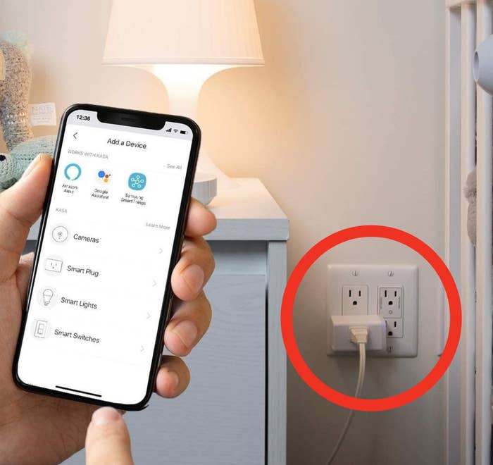 a person holding a phone next to a smart plug that is plugged into an outlet