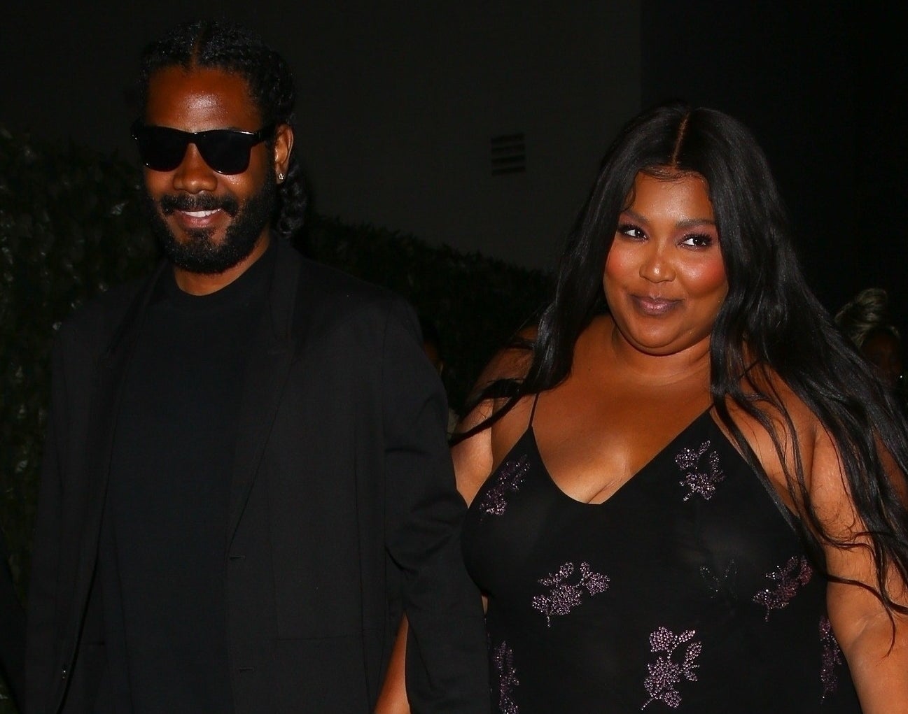 Lizzo smiles while standing close to a man in a black blazer and sunglasses