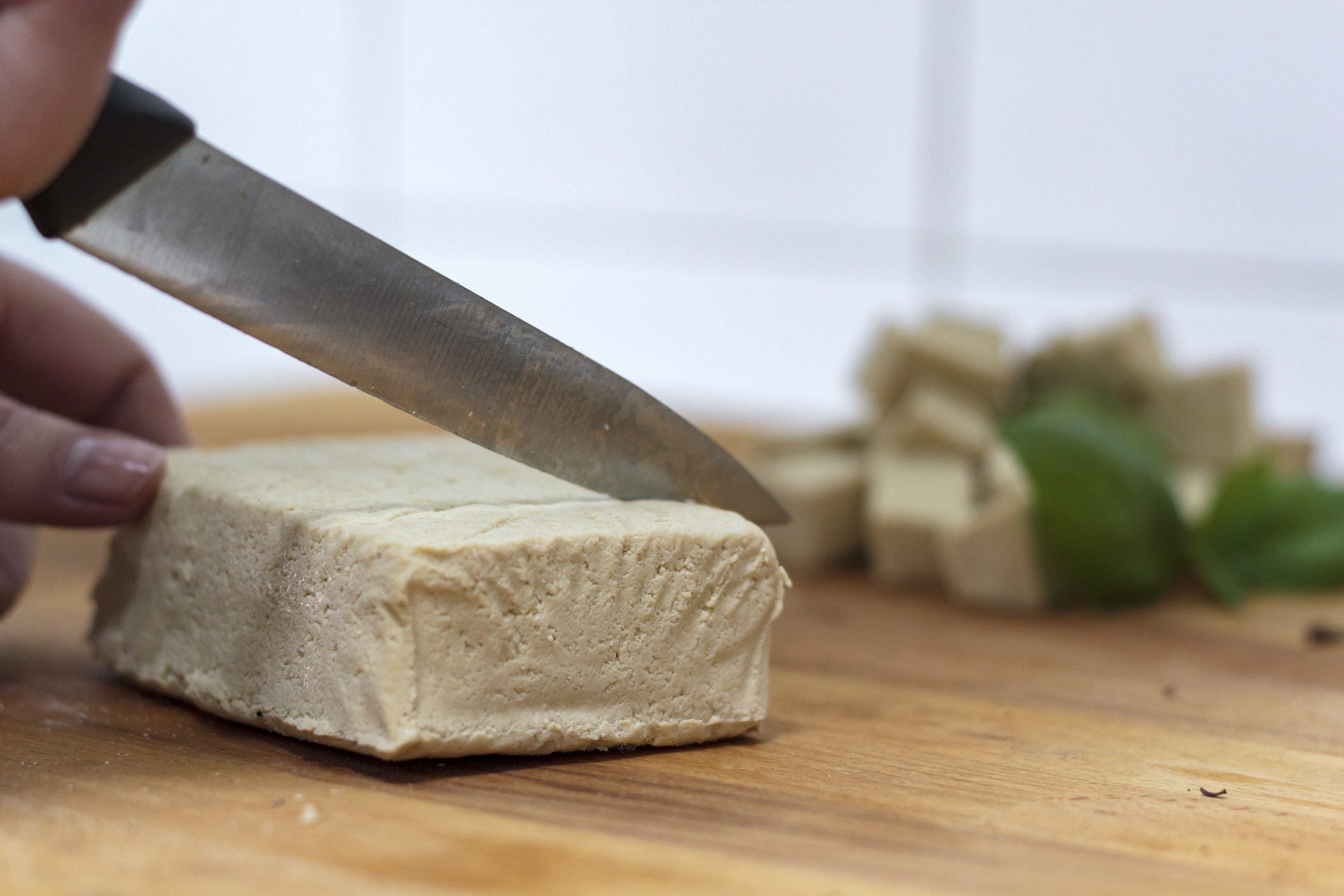 Woman with knife cutting firm tofu on wooden board
