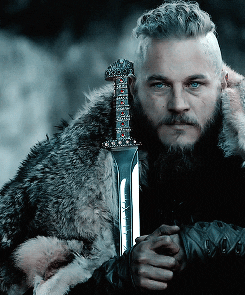 Travis Fimmel as Ragnar sitting down with a sword on his shoulder staring out into the distance