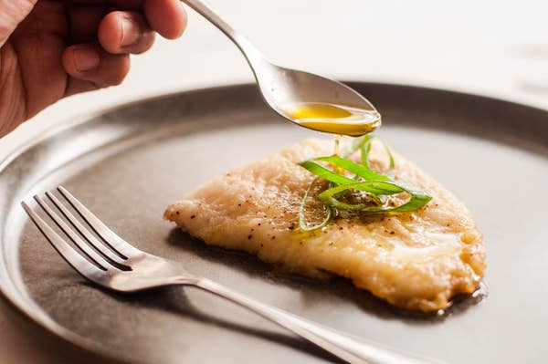 Pouring lemon butter onto a plate of fish