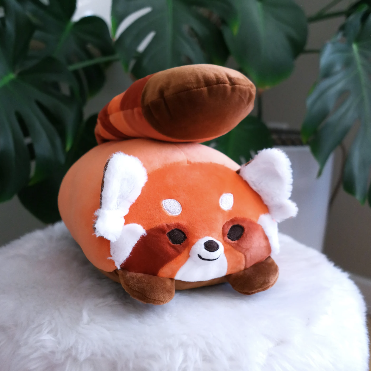 Red panda plush lounging on a fuzzy stool