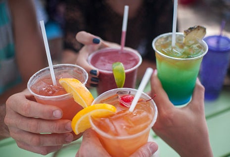 People hold tropical drinks in plastic cups