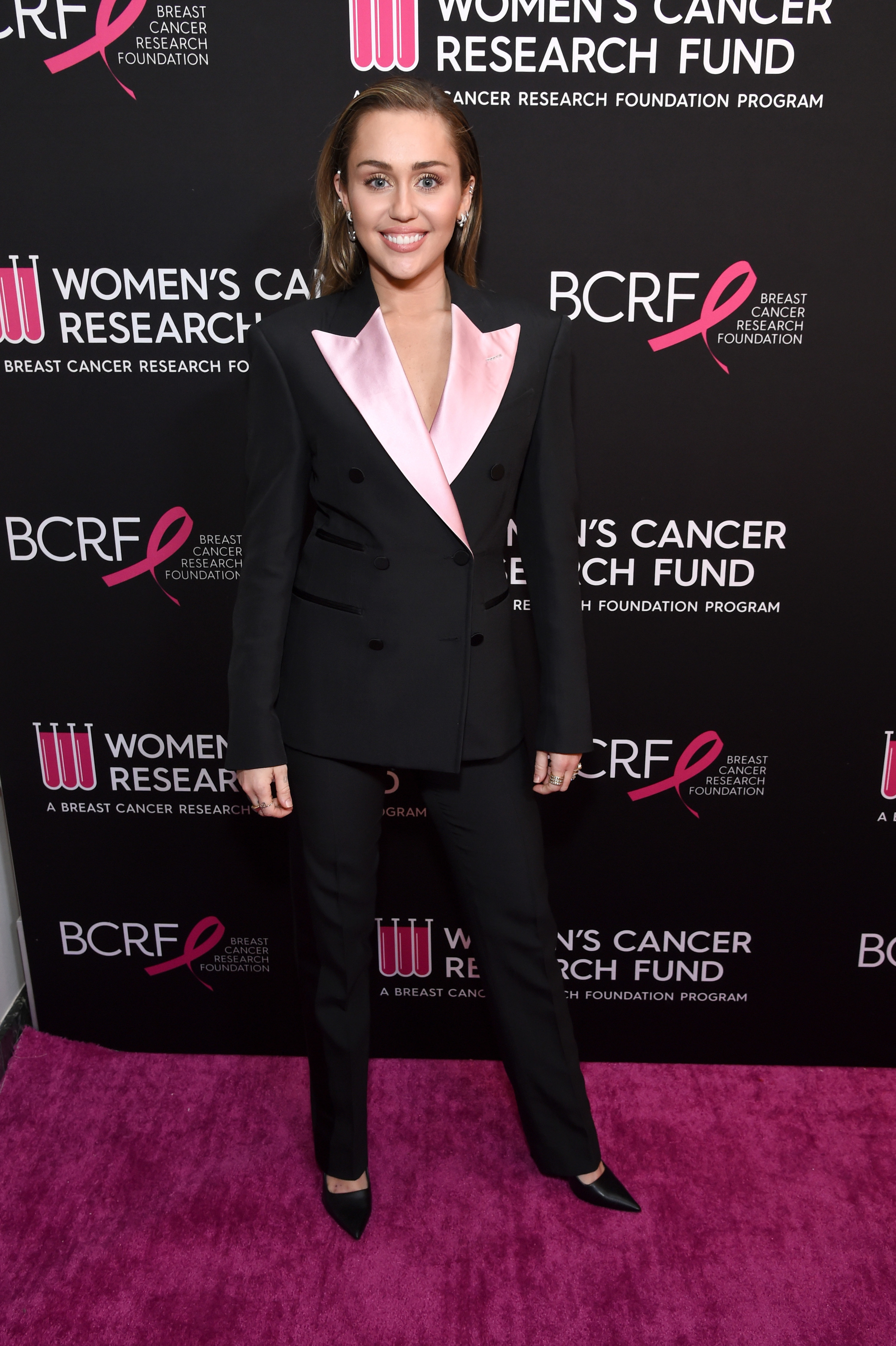 Miley Cyrus attends WCRF&#x27;s &quot;An Unforgettable Evening&quot; at the Beverly Wilshire Four Seasons Hotel on February 28, 2019 in Beverly Hills, California. She wears a black fitted suit with baby pink lapels, a double breasted blazer and pointy-toed high heels.