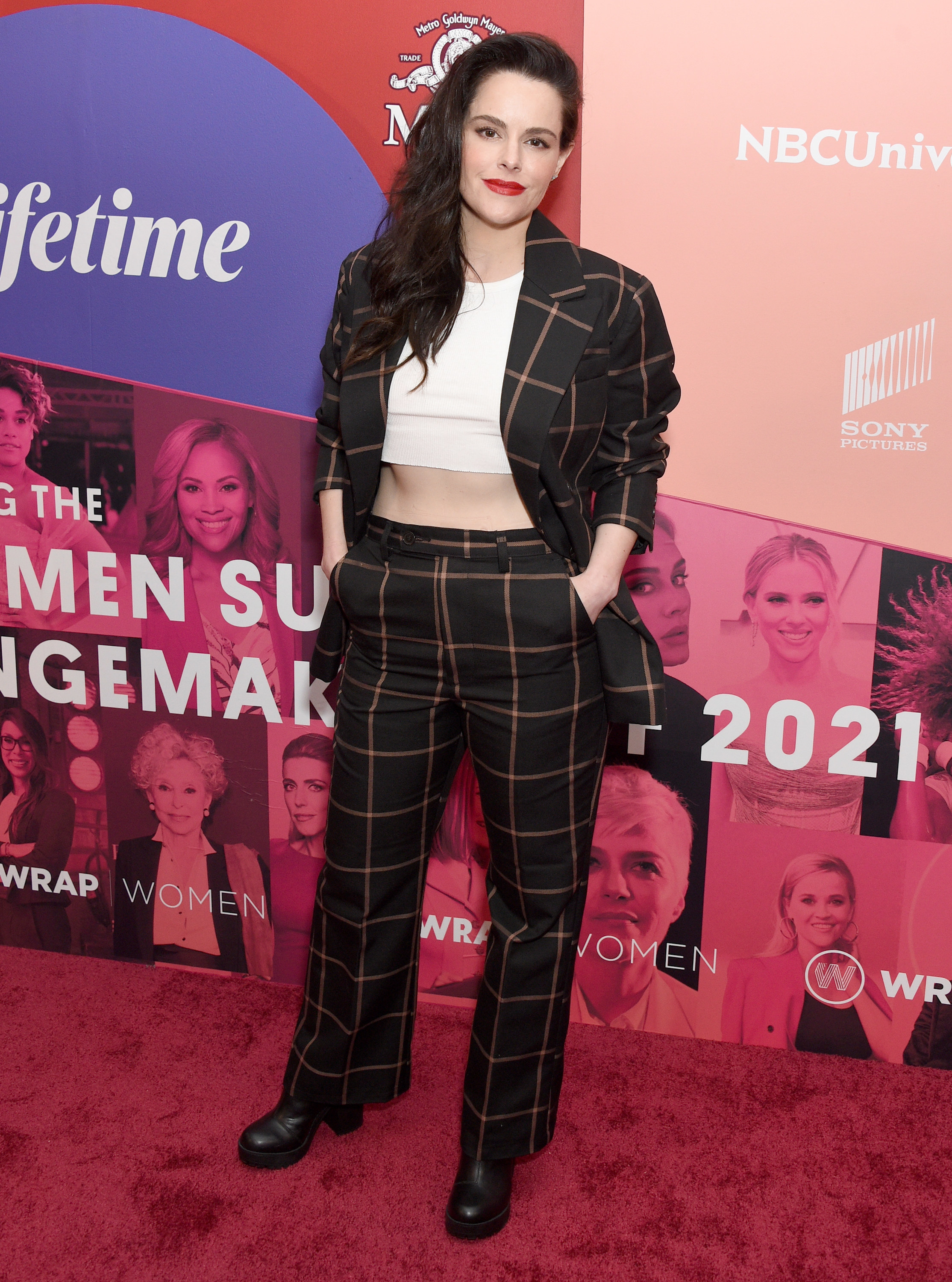 Emily Hampshire attends the WrapWomen&#x27;s Power Women Summit &amp; The Changemakers Of 2021. She wears a black suit with brown plaid pattern, with a white crop top underneath and chunky black boots.