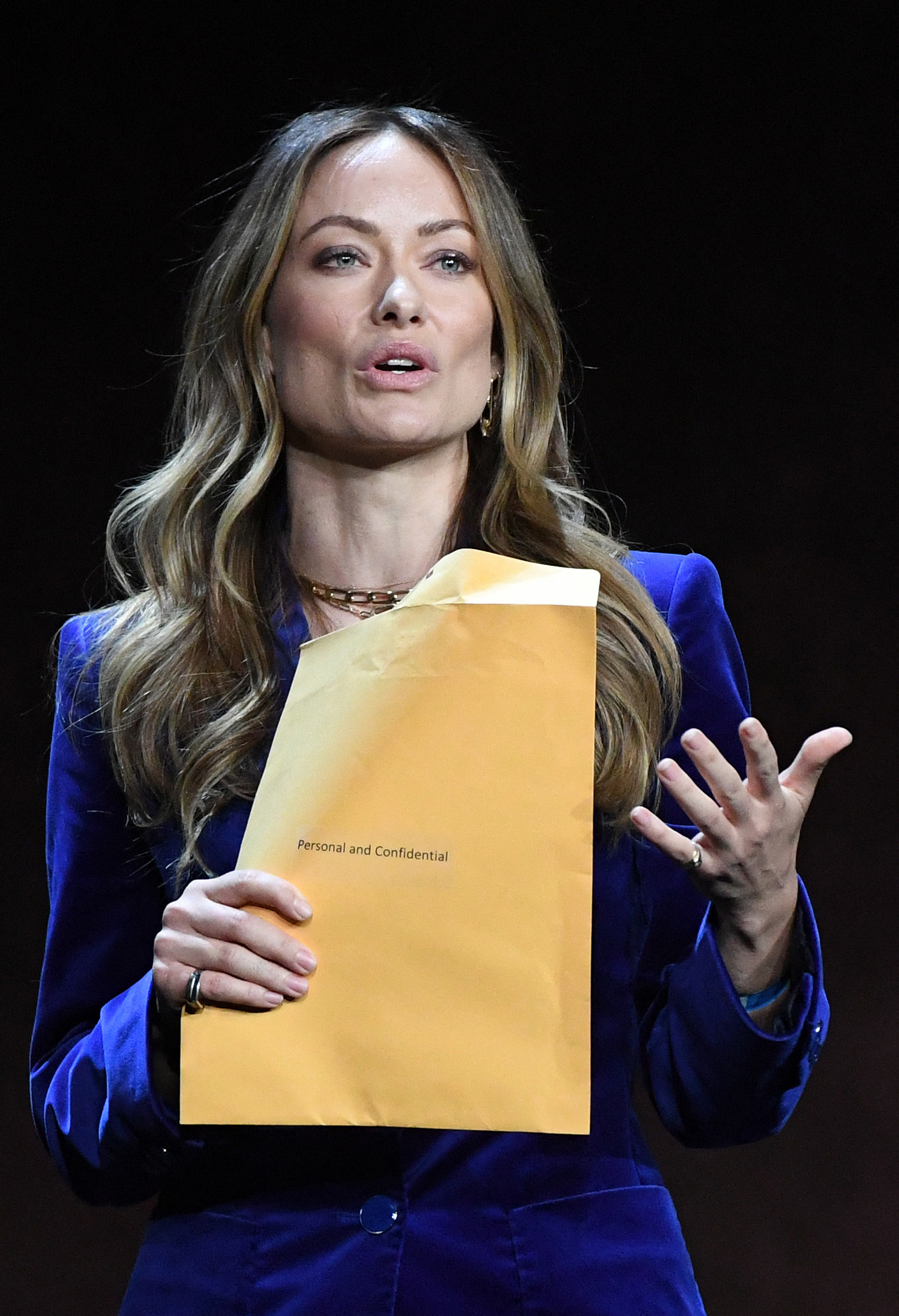 Olivia speaks while holding an envelope