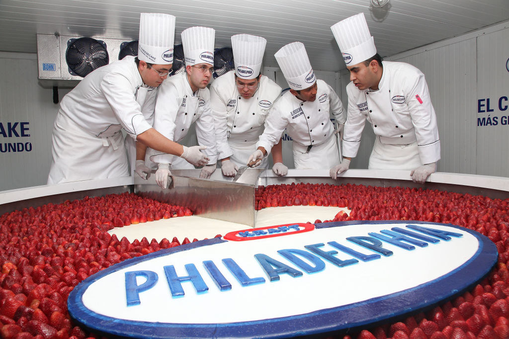 A mixing vat of strawberries and cream cheese with the Kraft Philadelphia logo on the mixer and men in chef uniforms around it