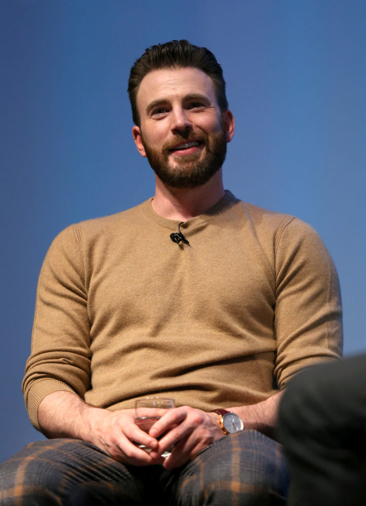 Smiling Chris with a mustache and beard, sitting and holding a glass