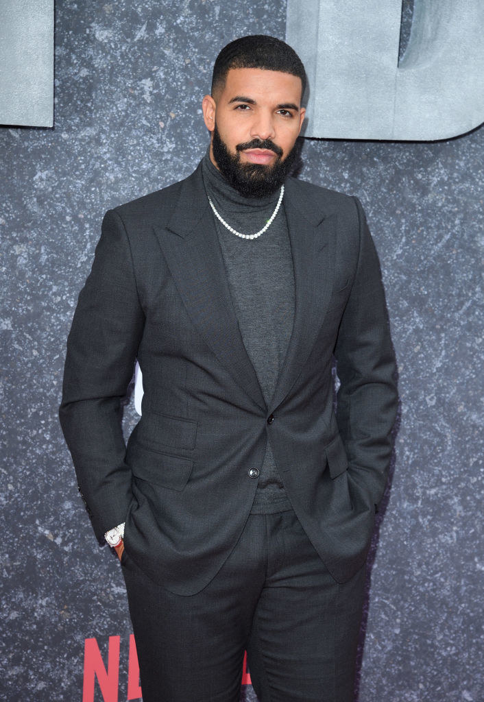 Drake with a mustache and heavy beard in a suit and turtleneck