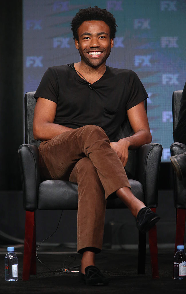 Smiling Donald with stubble and wearing a T-shirt, sitting with legs crossed