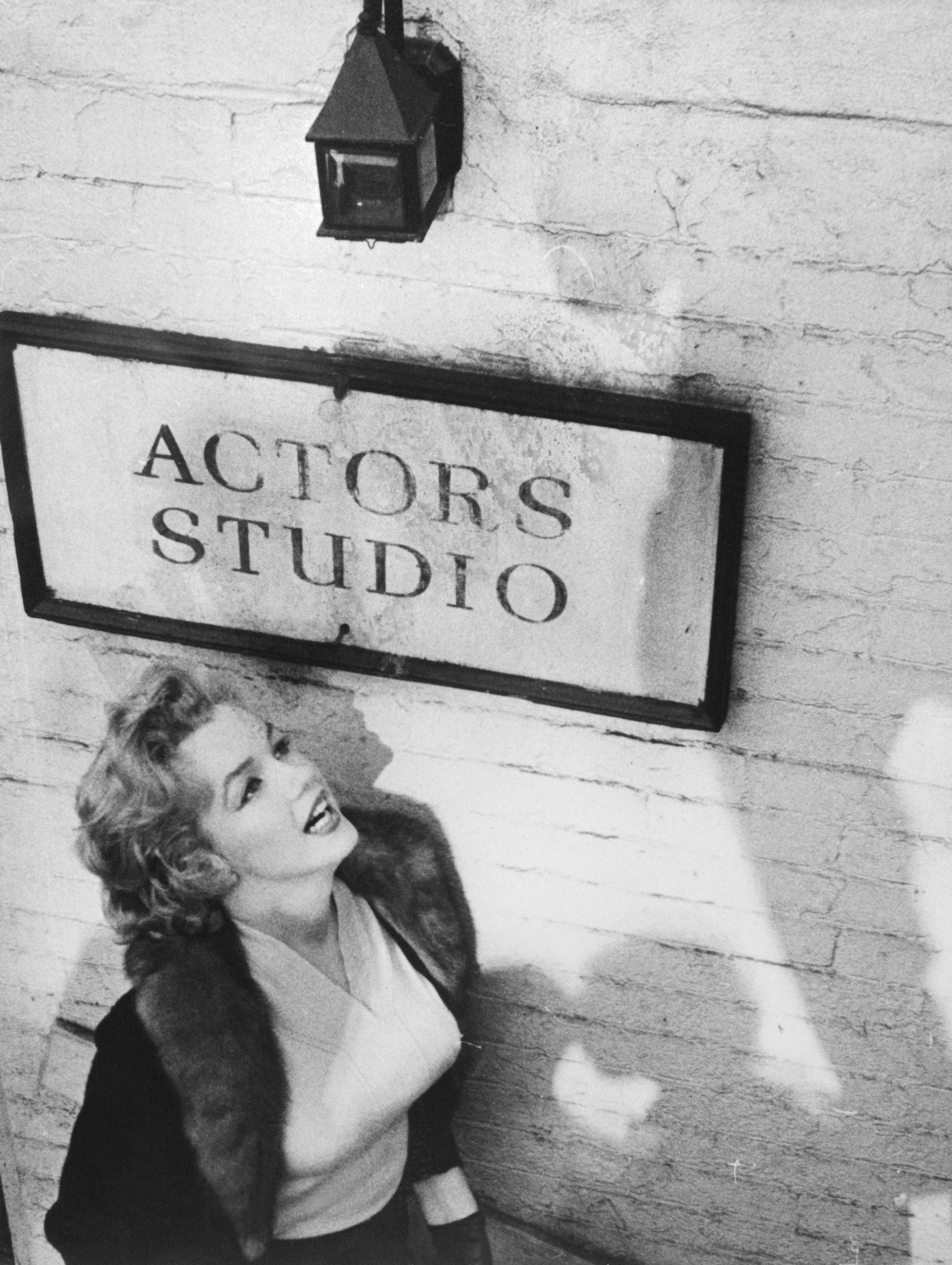 Marilyn Monroe stands by a sign outside of the Actors Studio