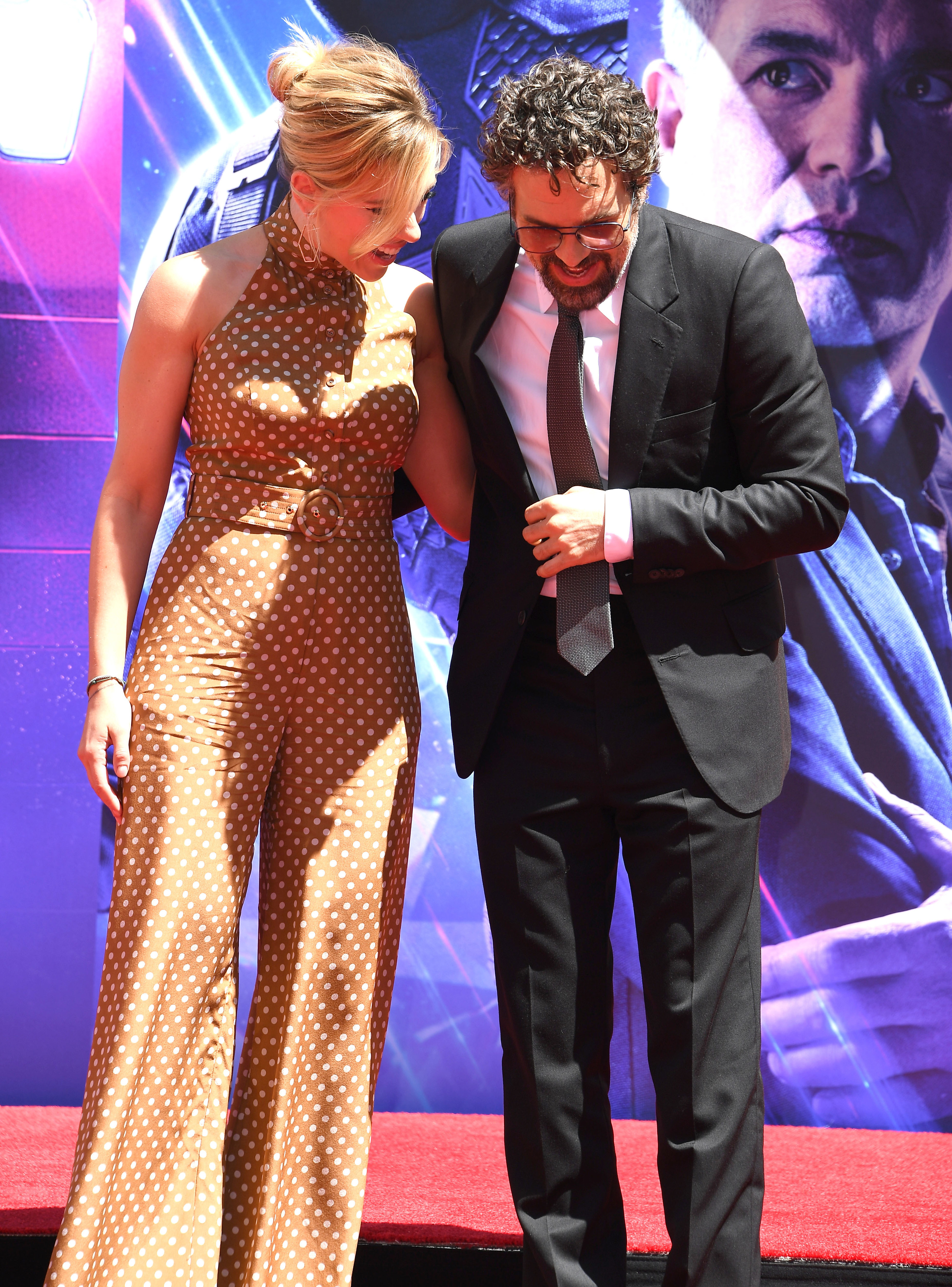 Scarlett with Mark Ruffalo. She wears a light brown polka dot jumpsuit with white dots. It has no sleeves, a high neck, flared trousers and a cinched in waist with a circular buckle.