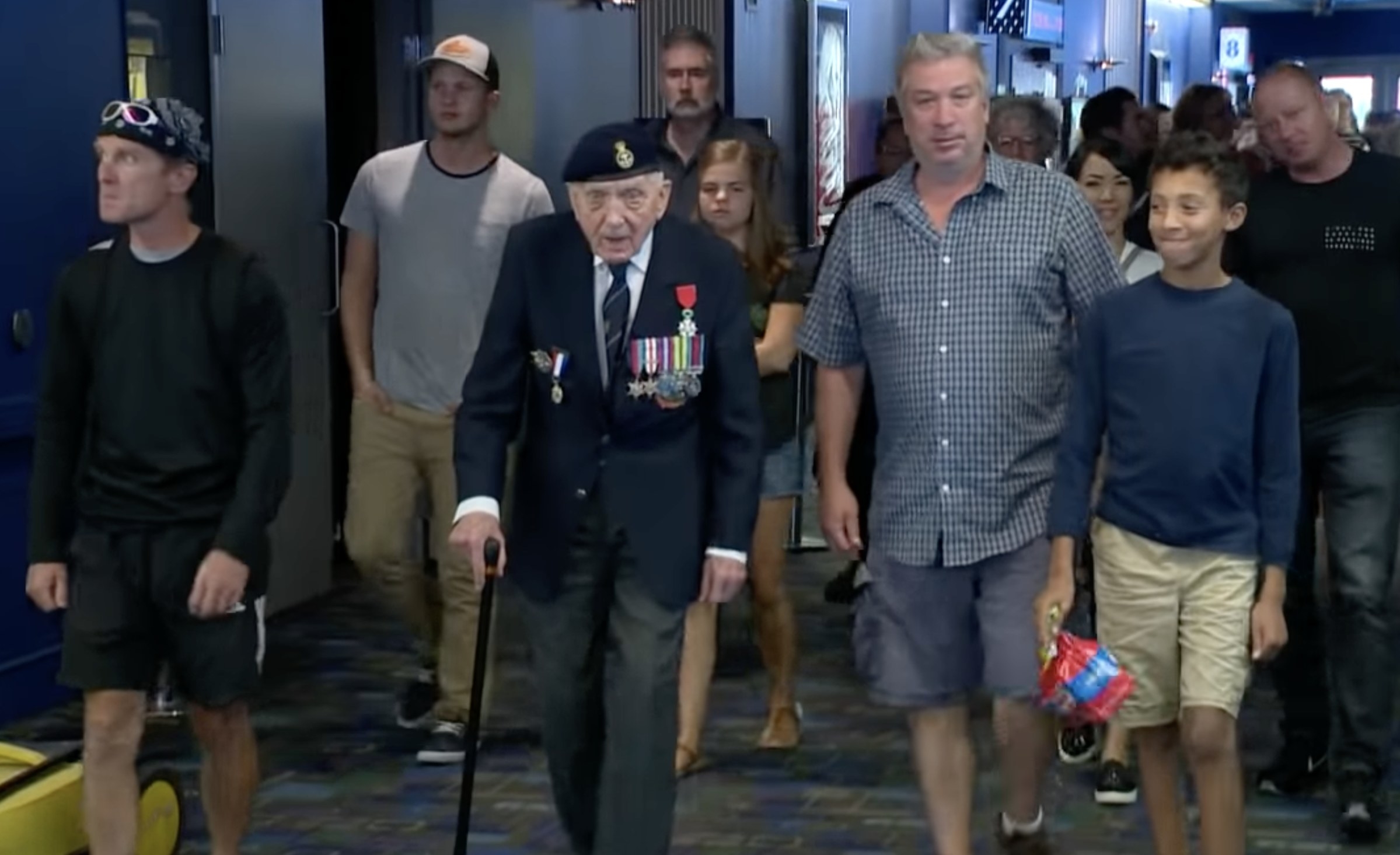A WWI veteran walks through a movie theater hallway with family around him