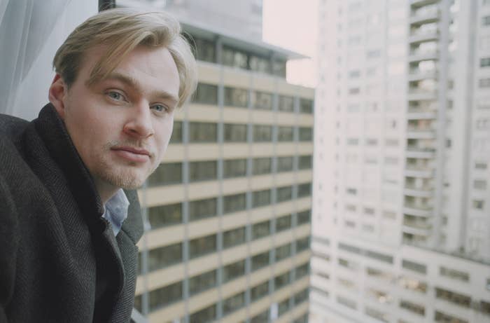 Christopher Nolan standing on a balcony in a city looking into the camera