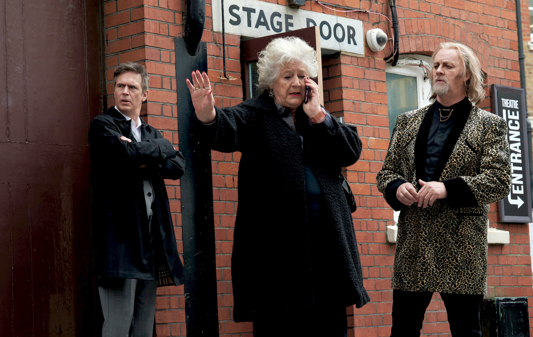Jack Davenport as Jonathan, Maggie Steed as Stella, and Tim McInnerny as Simon all stand outside a theatre entrance looking exasperated